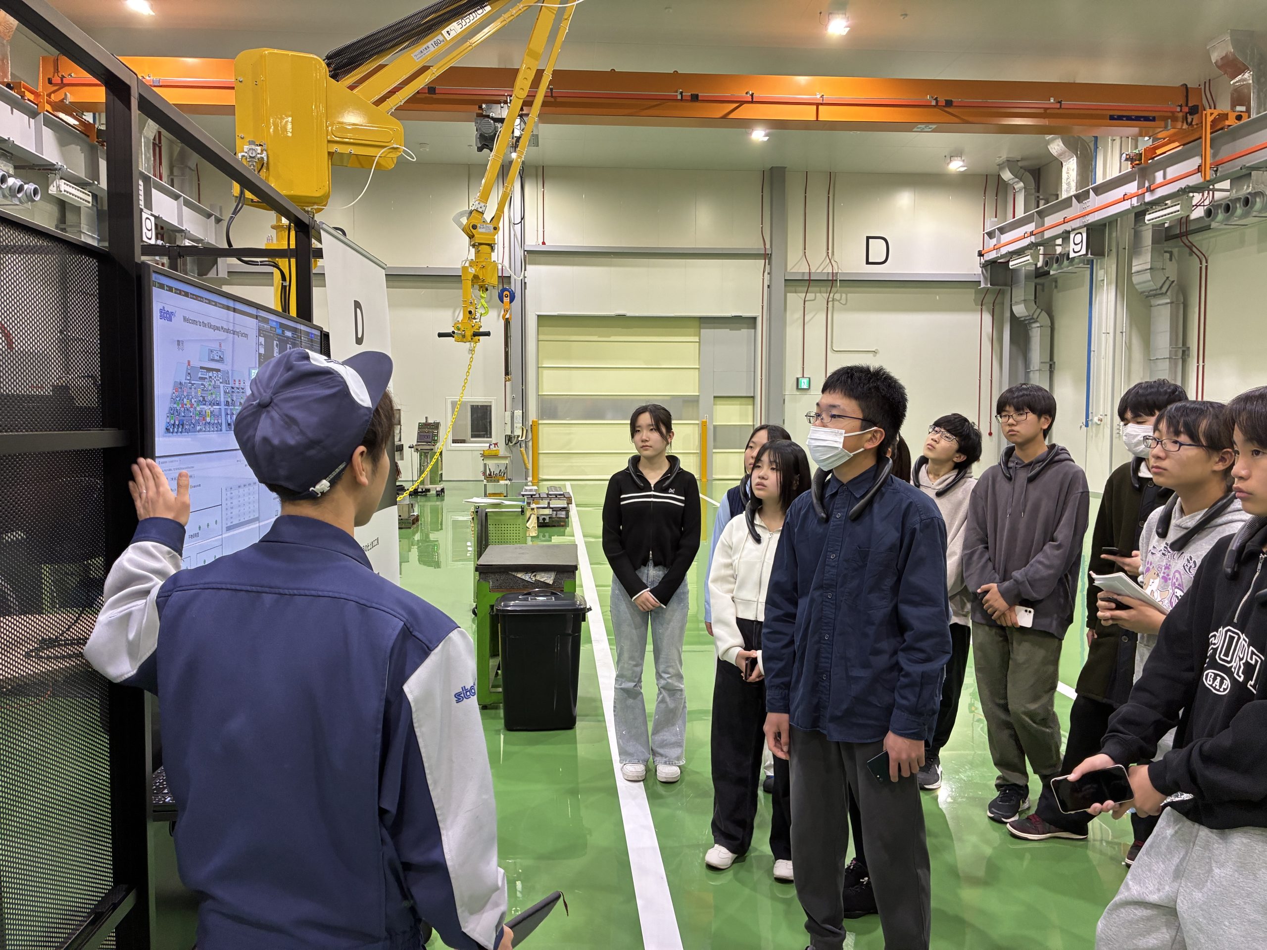 工場内で社員の説明を聞く学生たち