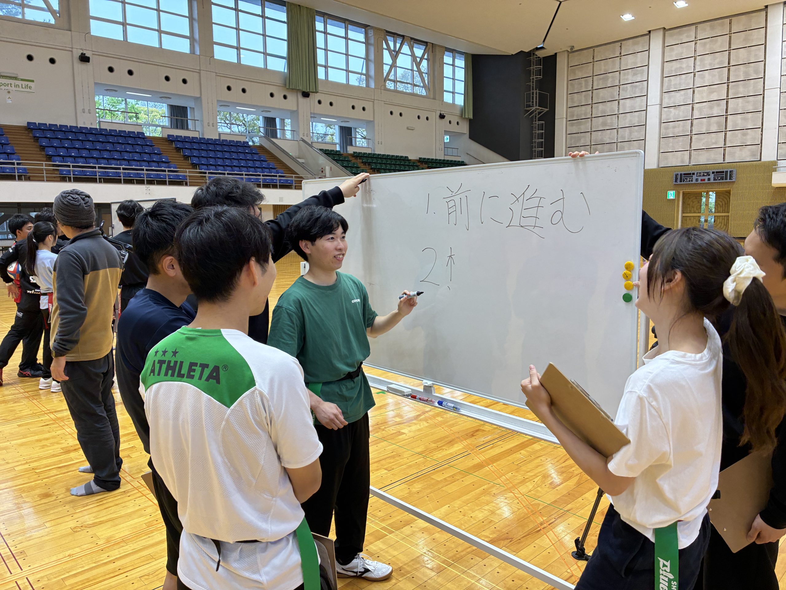 体育館のホワイトボード前でラグビーの指導を受ける参加者たち